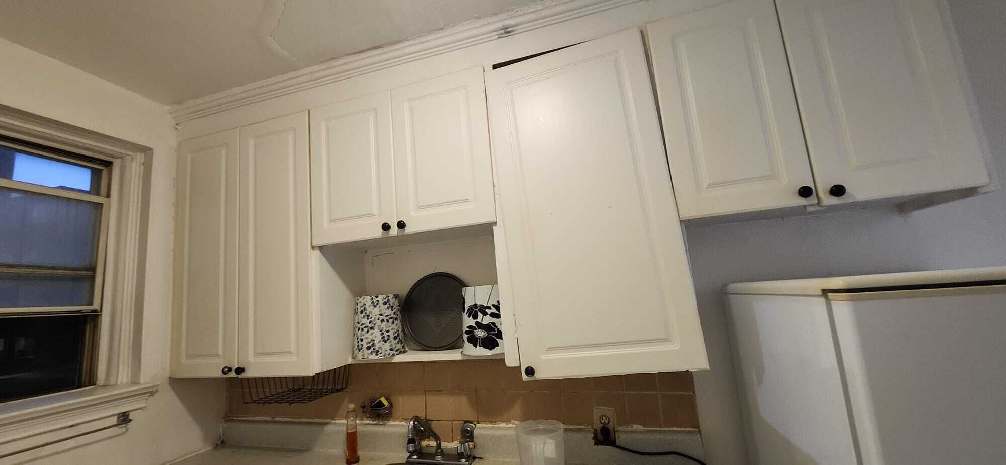 A kitchen with white cabinets, a window, a microwave, and a refrigerator.