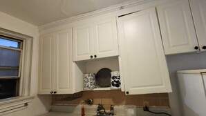 Eine Küche mit weißen Schränken, einem Fenster, einer Mikrowelle und einem Kühlschrank.