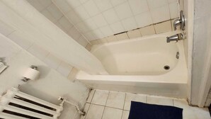 Ein kleines Badezimmer mit weißen Fliesen, einer Badewanne, einer Toilette und einem Heizkörper.