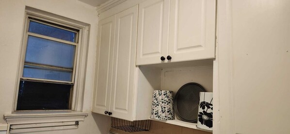 Una cocina con armarios blancos, una ventana con persianas y una repisa con utensilios de cocina.