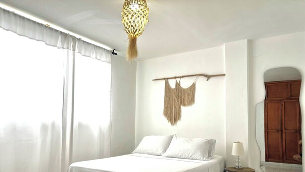 A bedroom with a bed, a bedside table with a lamp, a hanging macrame decoration, and a wardrobe. - Balconee Big Apartment Centre (Santa Marta)