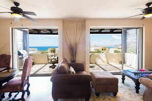 A living room with a sofa, armchair, and ottoman, a coffee table, and a ceiling fan. There is a view of the ocean through large glass doors. - 3-bedroom charming Villa in Cabo San Lucas, Mexico (Cabo San Lucas)