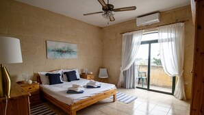 A bedroom with a wooden bed, a ceiling fan, a painting on the wall, and a view through the window. - ROOFTOP HIDEAWAY, JACUZZI, BBQ & PETss (L-Għarb)