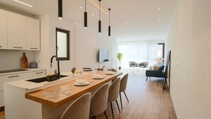 Una cocina moderna con una isla central, iluminación colgante y una zona de comedor con sillas y una mesa.