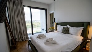 Una habitación de hotel moderna con una cama grande, vistas a través de una puerta corrediza de vidrio y una mesita de noche pequeña con una lámpara.