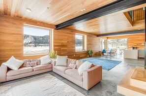 Ein geräumiger Wohnbereich mit einer großen, winkelförmigen Couch, einem Esstisch mit Stühlen und einer durch eine offene Tür einsehbaren Küchenzeile.