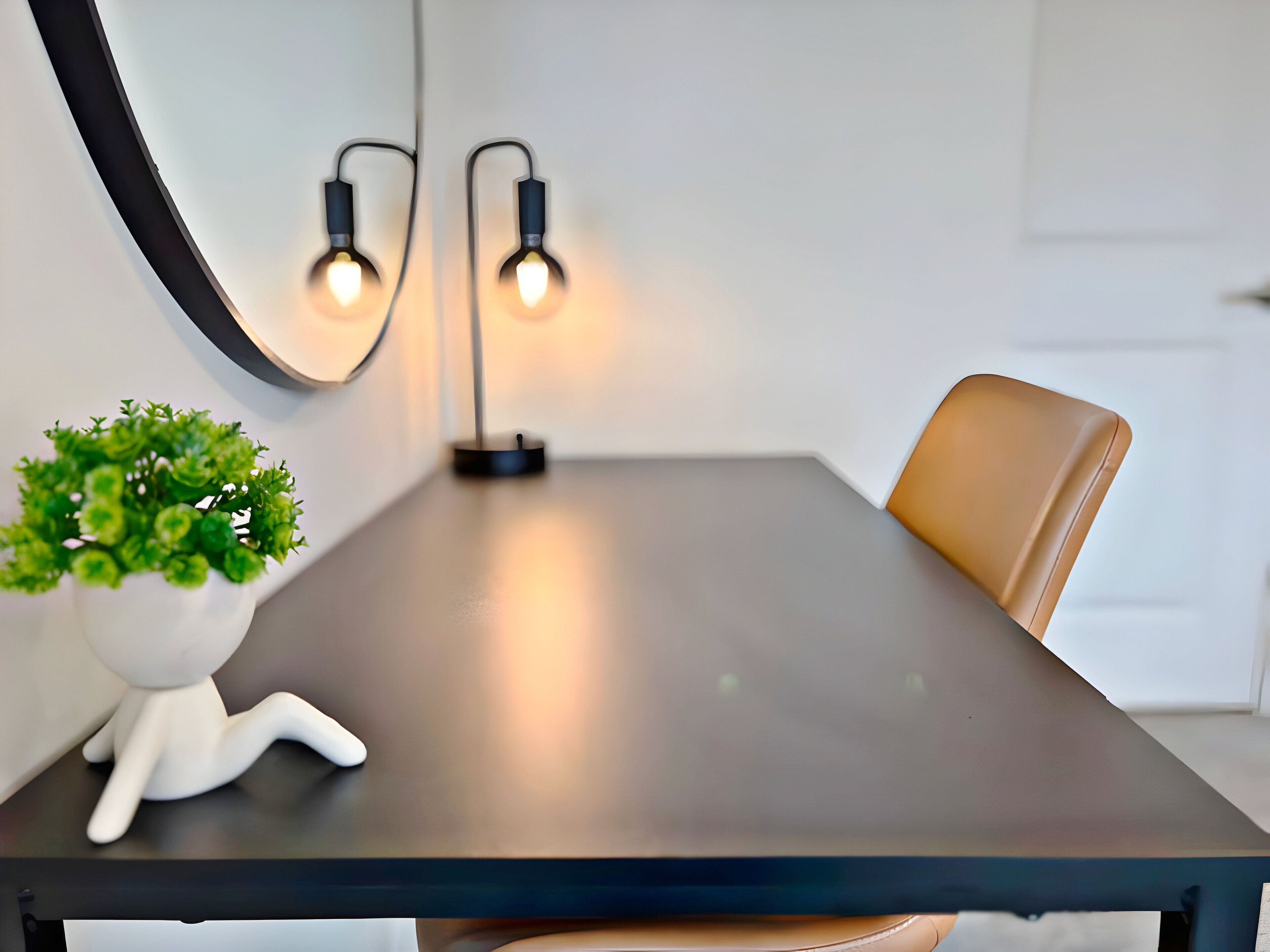 A modern dining table with two wall-mounted lights, a potted plant, and a leather chair.