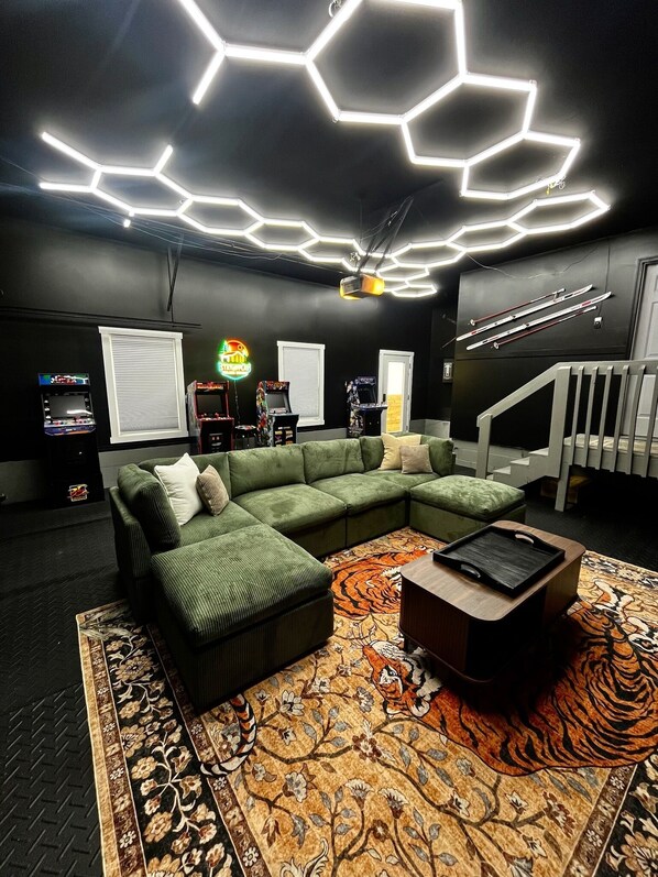 Un soggiorno moderno con un divano angolare verde, un tappeto decorato e un soffitto con lampade geometriche.