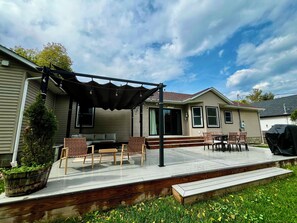 Una veranda coperta con mobili da esterno, un barbecue e un grande vaso di fiori.