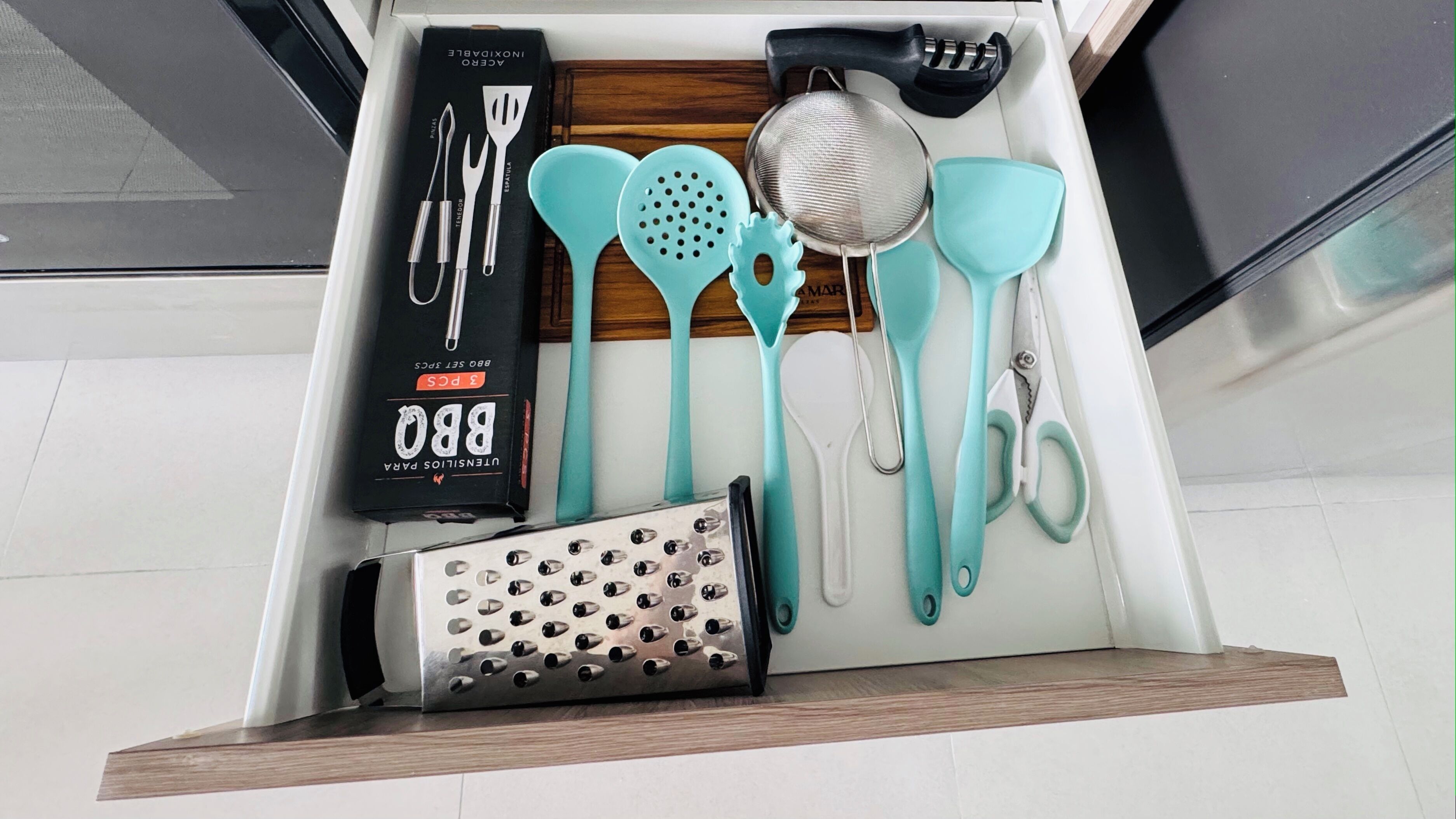 Un tiroir contenant des ustensiles de cuisine, notamment une râpe, des spatules, une passoire et une boîte d’ustensiles pour barbecue.