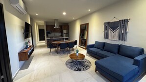 Ein modernes Wohnzimmer mit einem blauen Sofa, einem Essbereich mit Tisch und Stühlen sowie einer Küche im Hintergrund.
