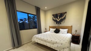 Ein ordentlich eingerichtetes Schlafzimmer mit einem großen Bett, einem Kopfteil mit dekorativer Dekoration, einem Nachttisch mit Lampe und einem Fenster mit Vorhängen.