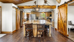 A spacious kitchen with a large island, wooden flooring, and a rustic ceiling.