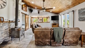A cozy living room with a stone fireplace, leather sofas, a ceiling fan, and a large clock on the wall.