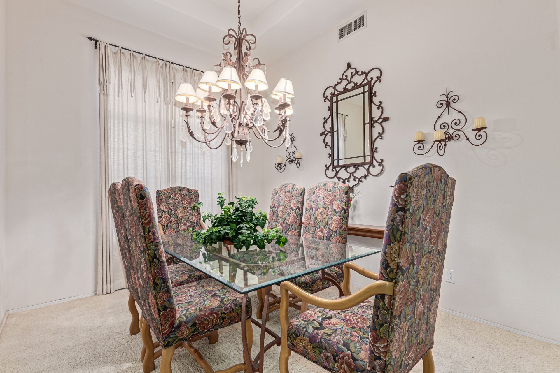 Un espace repas avec une table en verre entourée de chaises à motifs floraux, un lustre et des appliques murales.
