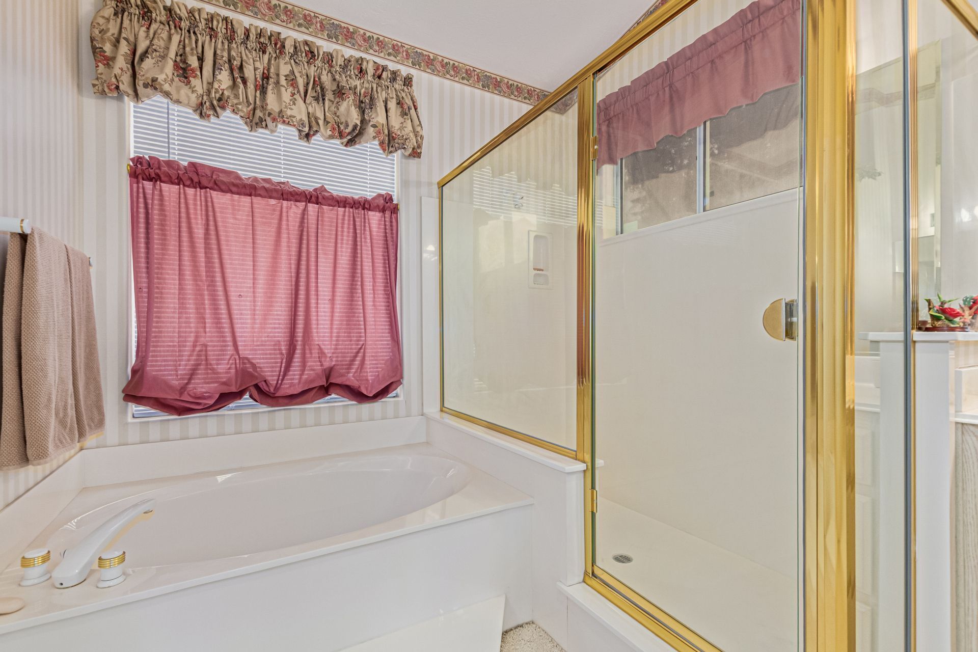 A bathroom with a bathtub, a glass shower enclosure, and a window with floral curtains.
