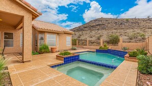 A house with a swimming pool, surrounded by a landscaped garden and a hilly landscape.