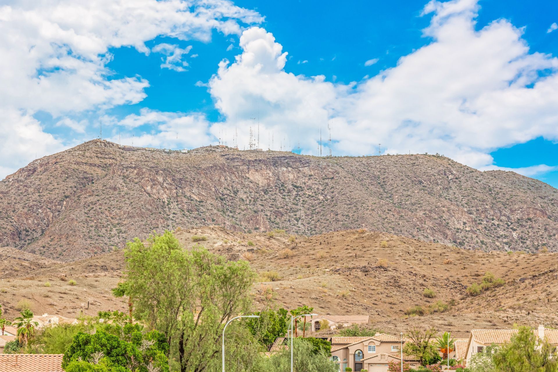 Un paisaje montañoso con una zona residencial en primer plano, que muestra casas con tejados de tejas y abundante vegetación.