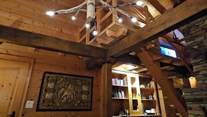 Un intérieur chaleureux avec un plafond en bois, un luminaire original rappelant un arbre et un mur en pierre.