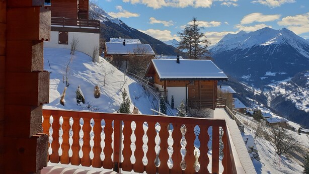 Un balcon en bois offrant une vue sur des montagnes enneigées et un ciel dégagé.