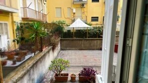 Un patio estrecho con plantas en macetas, una sombrilla blanca y un muro de hormigón.