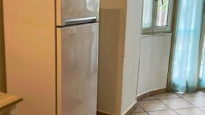 Una cocina con un refrigerador blanco, una ventana con cortina y piso de baldosas.