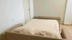 Una habitación pequeña con cama individual, cubierta con una colcha color beige y cabecera a juego.