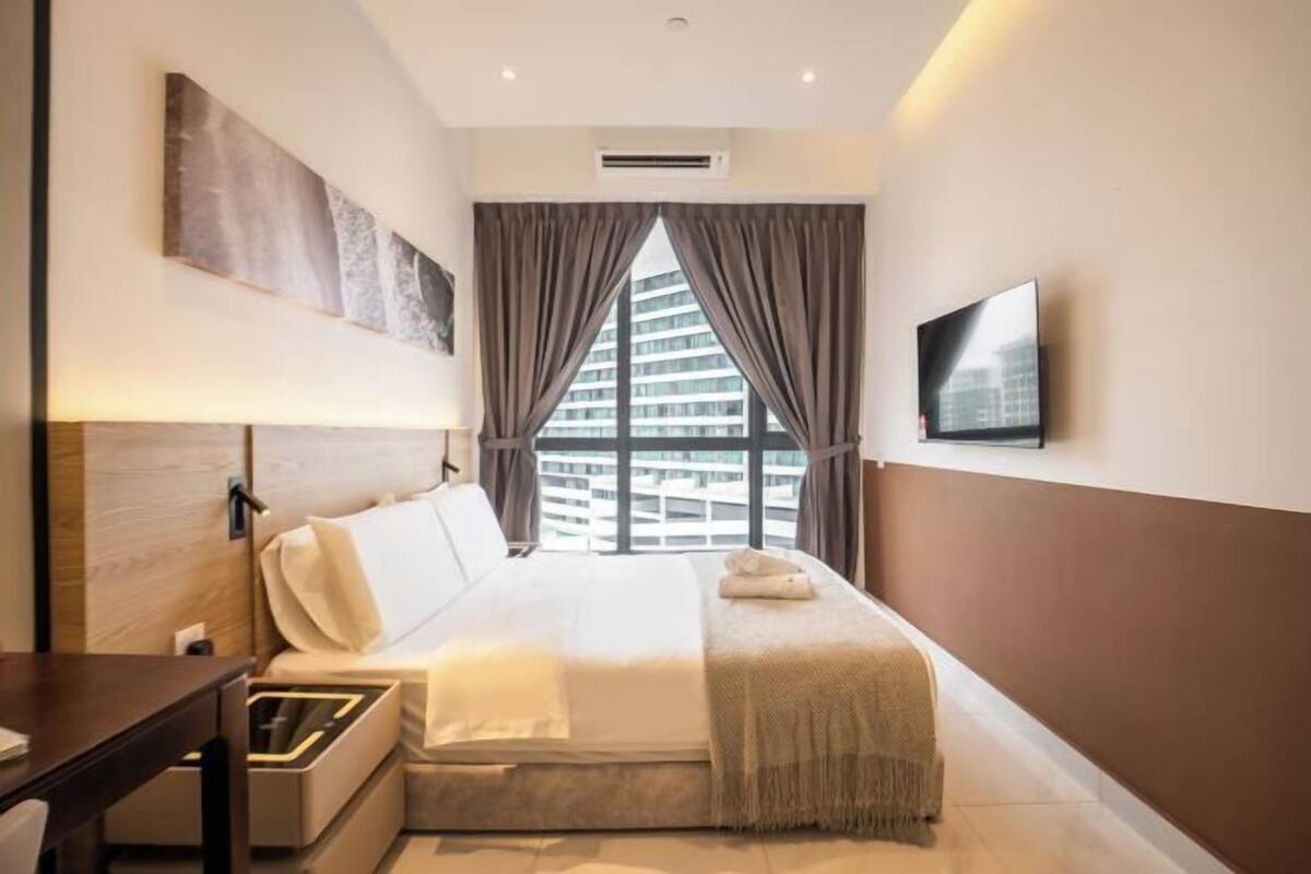 A hotel room with a bed, a desk, a TV, and a window with curtains.