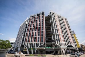 A multi-story building with a modern architectural design, featuring a prominent entrance with a curved overhang and a sign indicating a business or commercial use. - Inap II, Suterabay by Ayuhouz (Kota Kinabalu)