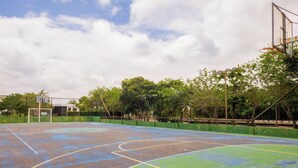 Un terrain de basket en plein air, entouré d’une clôture verte, avec des arbres et un ciel nuageux.