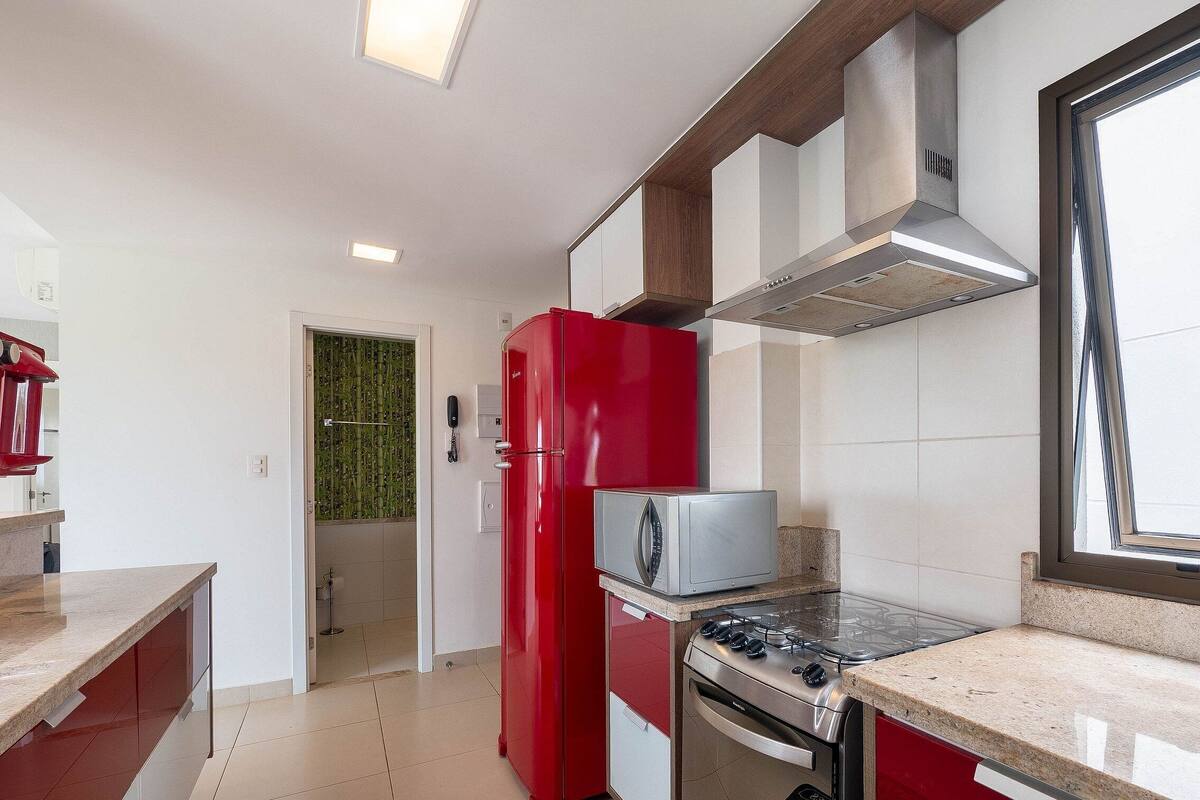 A modern kitchen with a red refrigerator, a built-in oven, and a gas stove.