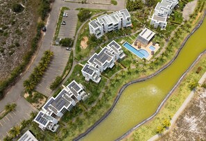 An aerial view of a modern residential complex with multiple buildings, a swimming pool, and a river.