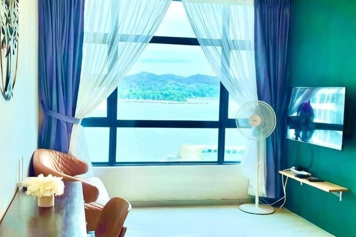 Una habitación con una ventana grande, un ventilador, un televisor y una cama.