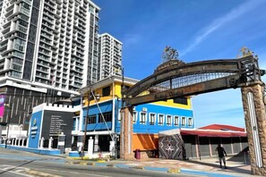 A multi-story hotel with a prominent entrance gate, a blue and yellow facade, and a large building in the background. - Jesselton Quay - Sunset Ocean View Apartments by Quality Home Living (Kota Kinabalu)