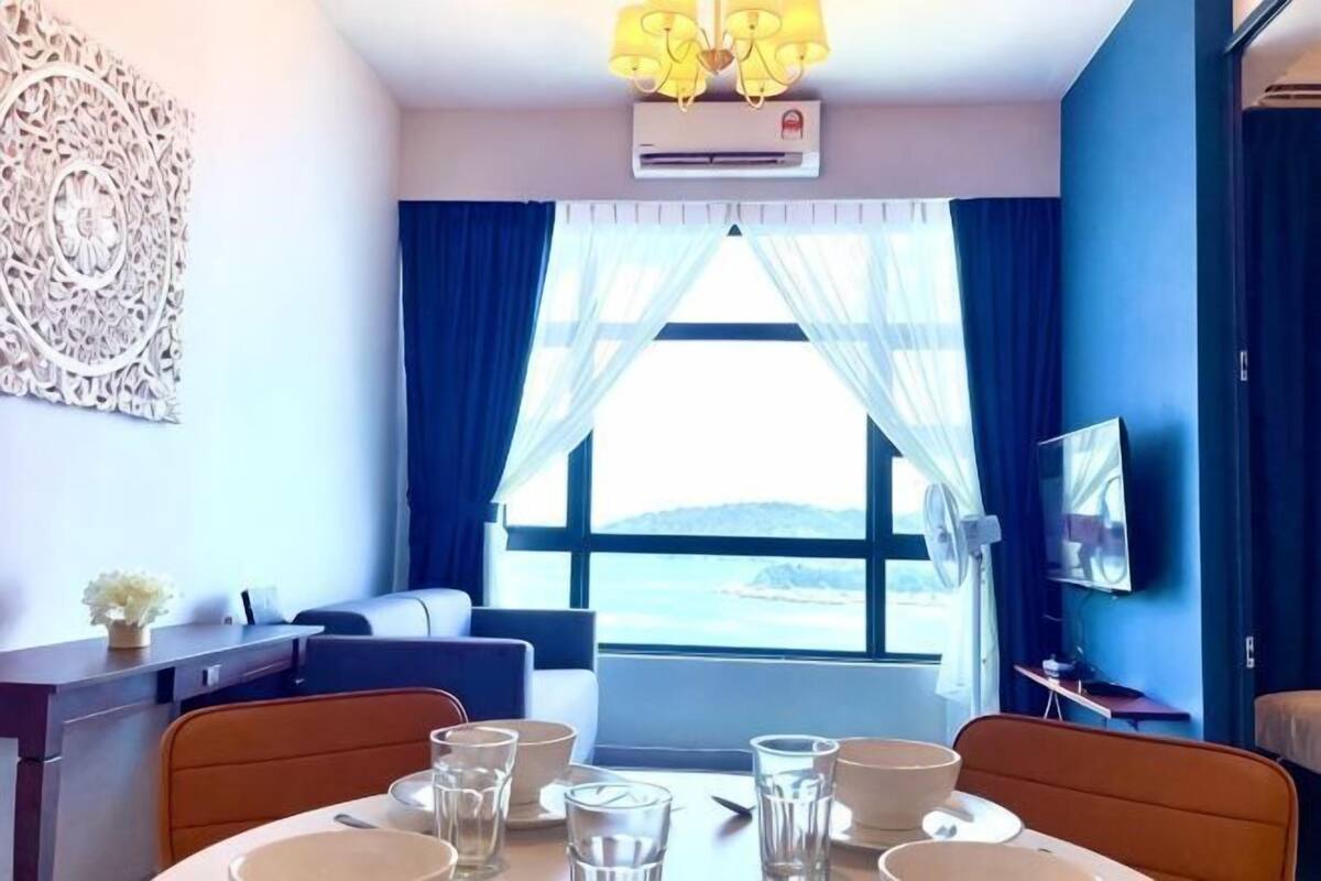 Habitación de hotel con mesa de comedor, sofá, televisor y un amplio ventanal con vistas.
