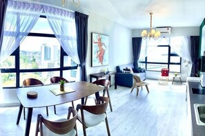 Et moderne hotelværelse med spiseplads, sofa, tekøkken og store vinduer med udsigt over byen.