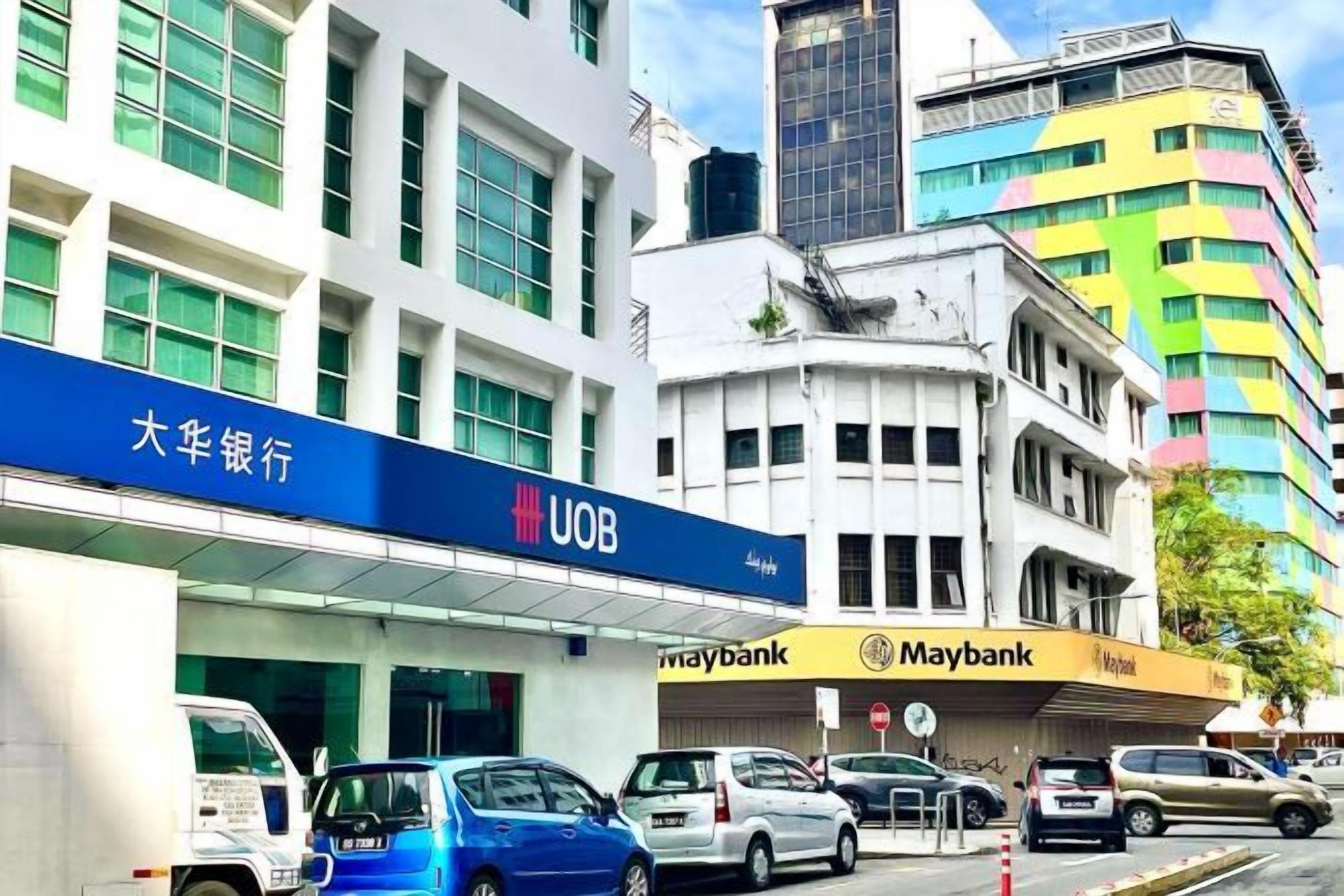 A commercial building with a UOB sign, a Maybank ATM, and several parked cars.