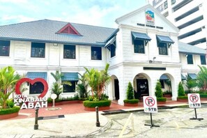 A building with a white facade, multiple windows, and a red roof. There are palm trees and a heart-shaped sign with text. - Jesselton Quay - Sunset Ocean View Apartments by Quality Home Living (Kota Kinabalu)