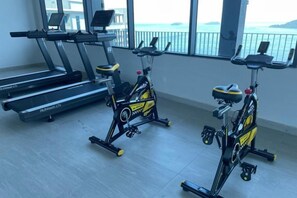 Un gimnasio con equipamiento de ejercicio, incluyendo cintas de correr y bicicletas estáticas, ventanas amplias con vista al mar.