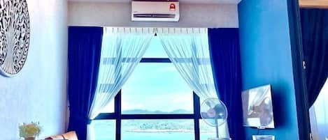 A room with a dining table, chairs, a chandelier, an air conditioning unit, and a large window with curtains.