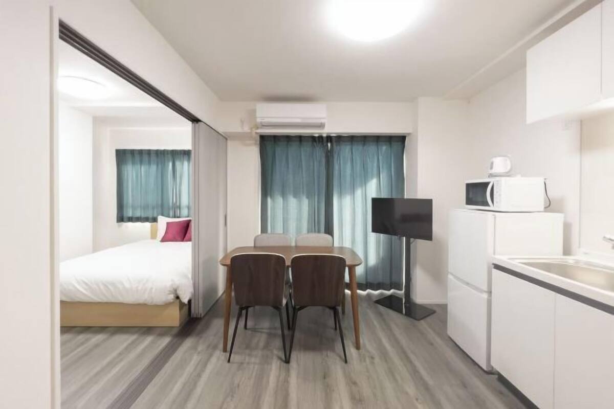Une chambre d’hôtel compacte comprenant un lit, une table à manger avec des chaises, un téléviseur à écran plat, un four à micro-ondes et une kitchenette.