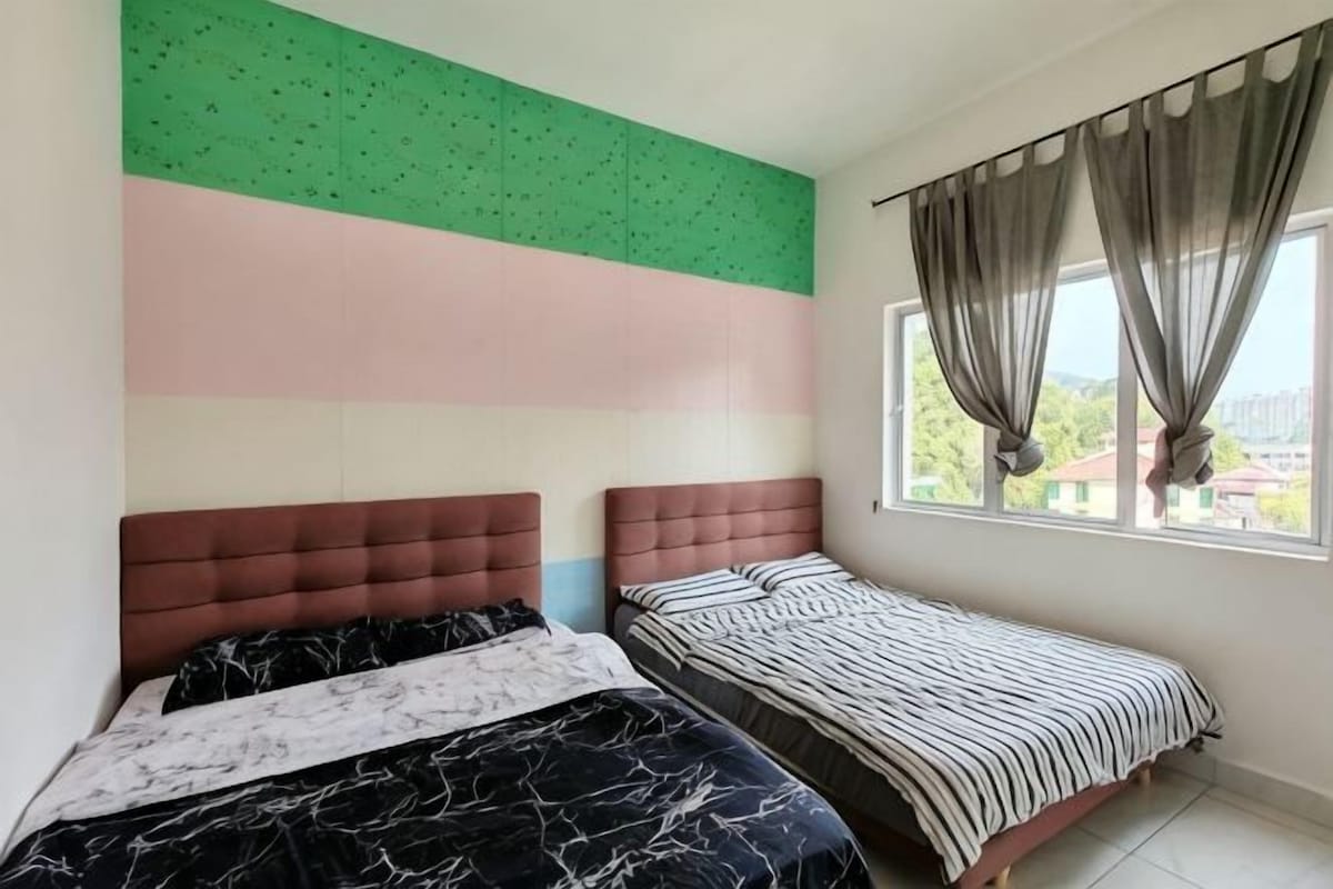A bedroom with two beds, a large window with curtains, and a wall with a green and pink design.