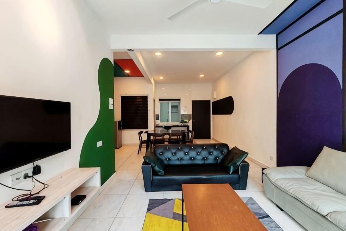 A modern living room with a black leather sofa, a wooden coffee table, a TV mounted on the wall, and a dining area in the background.