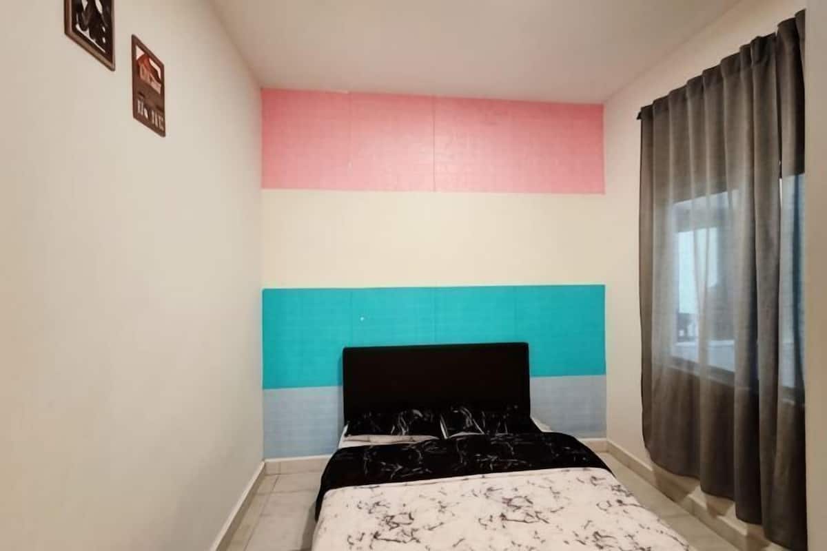A bedroom with a bed, a headboard, a window with curtains, and a wall with a color block design.