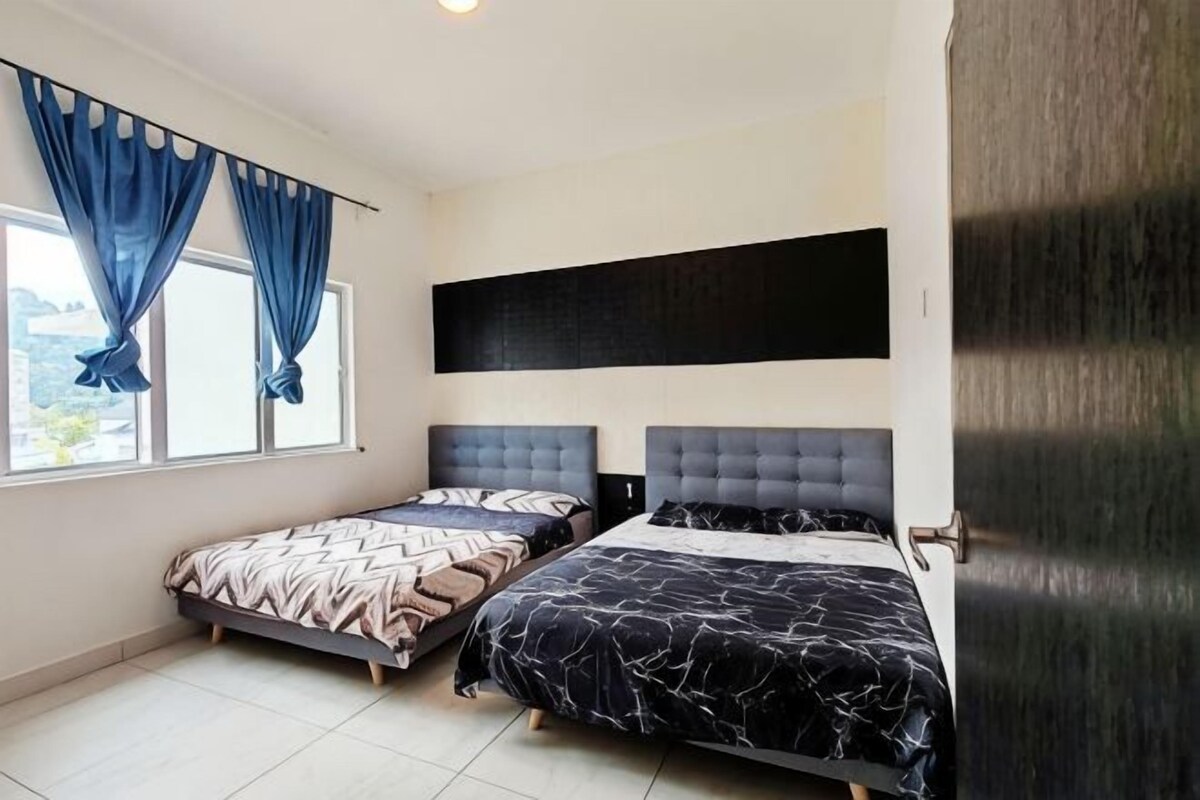 Une chambre avec deux lits, une fenêtre avec des rideaux, une tête de lit noire et une vue sur l’extérieur.