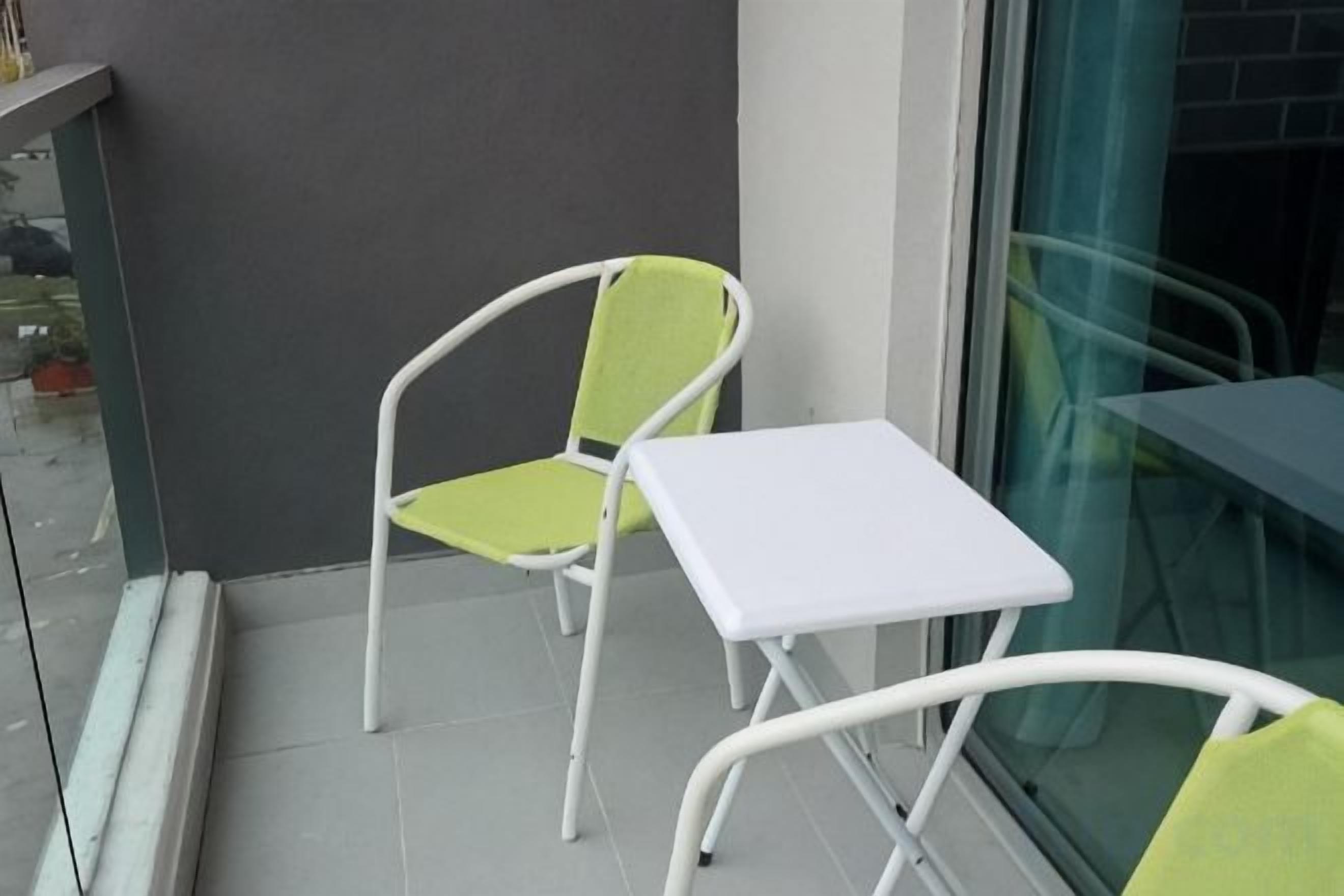 Un balcón con una mesa blanca y dos sillas, una de ellas con asiento verde.