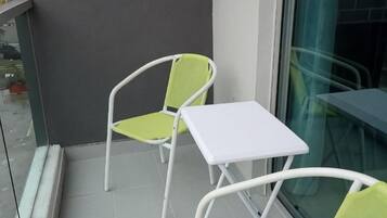 Un balcón con una mesa blanca y dos sillas, una de ellas con asiento verde.