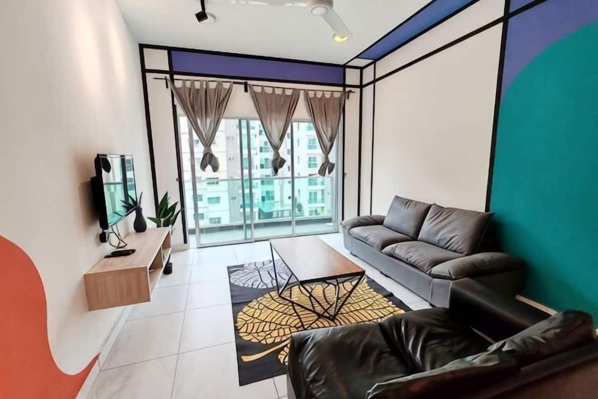 Una sala de estar moderna con un sofá, un televisor, una mesa de centro y vistas de edificios a través de amplias ventanas.
