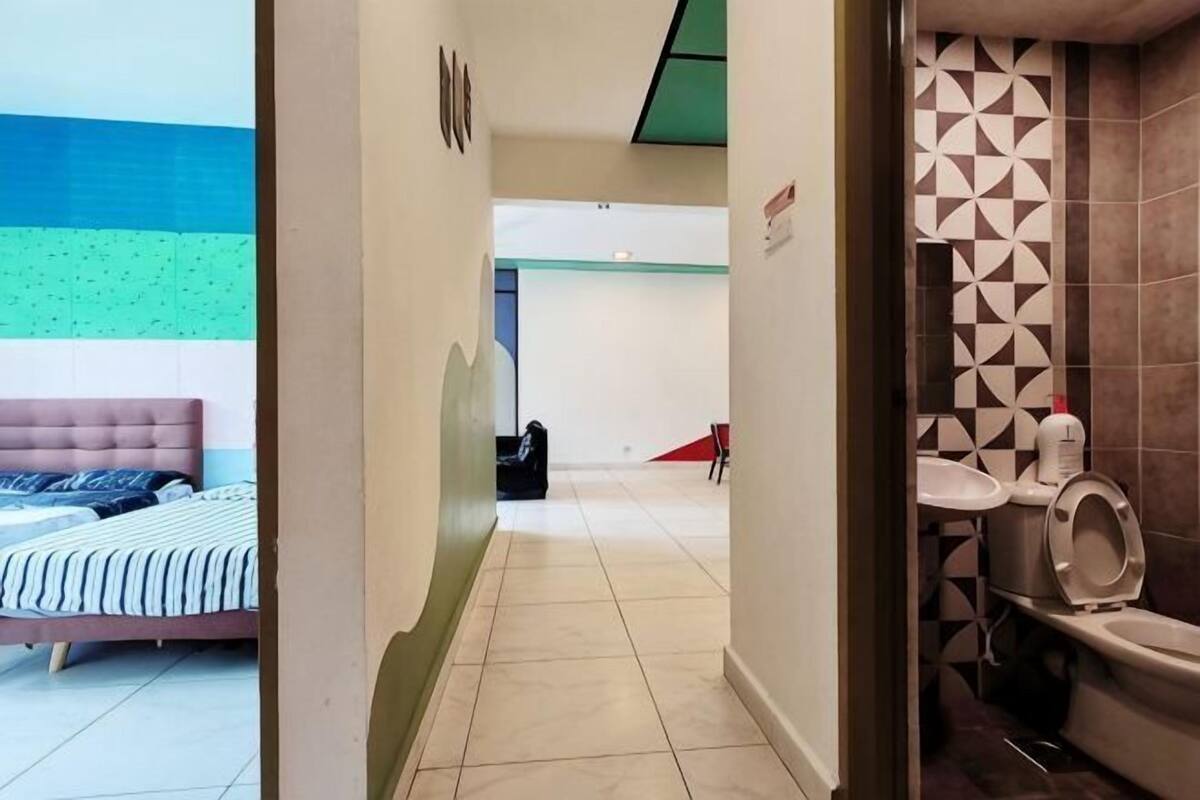 A hotel room with a bed, a bathroom with a toilet and sink, and a hallway leading to another room.