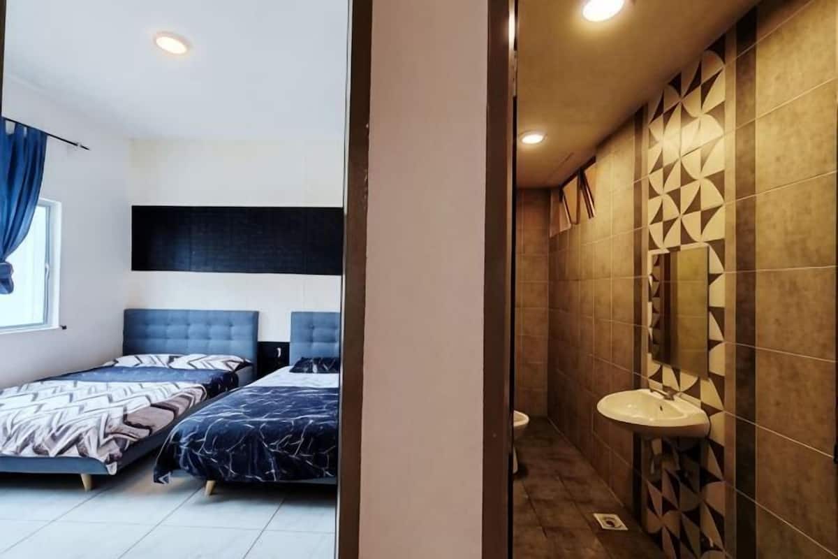 A bedroom with two beds, a window with curtains, and a bathroom with a sink and patterned tiles.